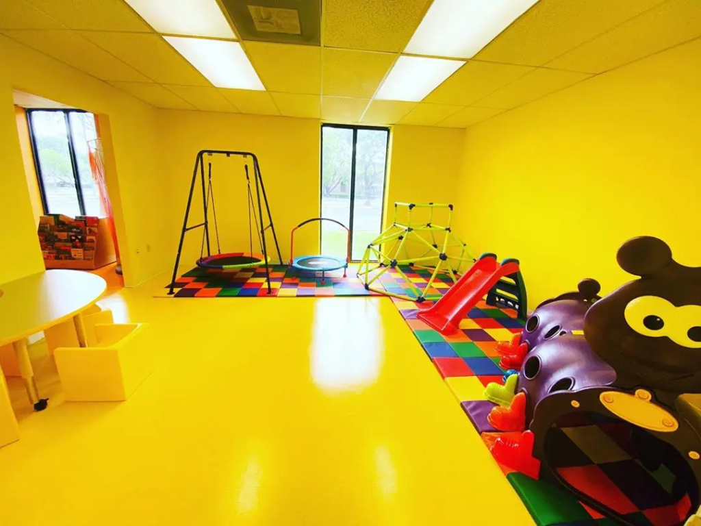 Brightly colored playroom equipped with swings, a trampoline, climbing structure, and slides, designed for children.