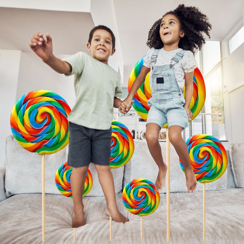 Two children joyfully jumping on a couch, holding hands, with large colorful lollipops in the background.